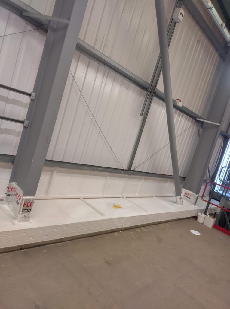 Wrapped steel column bases and white insulation boarding along the base of an industrial wall