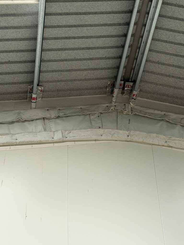Head-of-wall junction beneath a profiled roof deck, with insulated and wrapped service supports