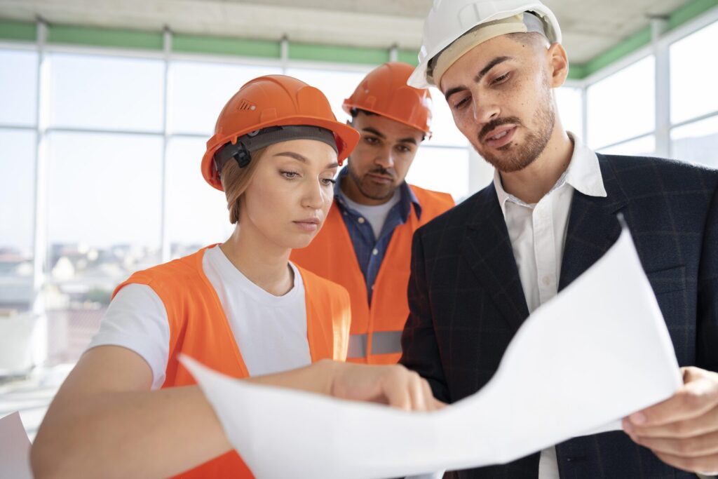 Three construction professionals in hard hats reviewing a building plan together