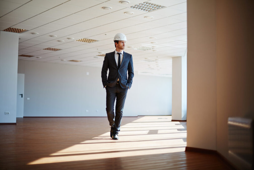 Man in a suit and hard hat walking through an empty open-plan office floor